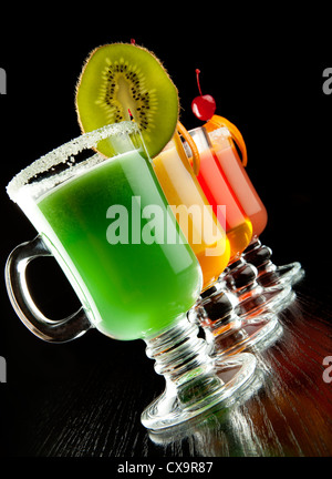 Groupe de quatre verres à vin avec des cocktails sans alcool coloré, décoré avec des fruits et du sucre sur comptoir de bar noir Banque D'Images