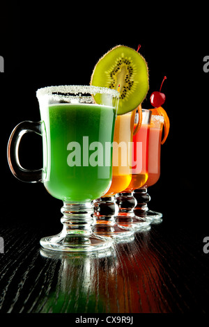 Groupe de quatre verres à vin avec des cocktails sans alcool coloré, décoré avec des fruits et du sucre sur comptoir de bar noir Banque D'Images