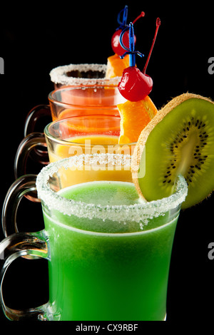 Groupe de quatre verres à vin avec des cocktails sans alcool coloré, décoré avec des fruits et du sucre sur comptoir de bar noir Banque D'Images