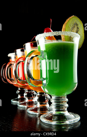 Groupe de quatre verres à vin avec des cocktails sans alcool coloré, décoré avec des fruits et du sucre sur comptoir de bar noir Banque D'Images