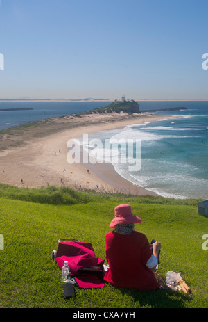 Woman wearing sunhat sitting rouge sur l'herbe de Fort Scratchley surplombant la plage de Nobbys et Newcastle NSW Australie phare Banque D'Images