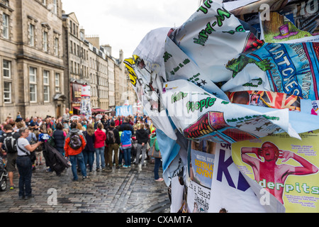 Voir les affiches couvrant poster sur le Royal Mile avec la foule entourant un interprète à l'Edinburgh Fringe Fest 2012 Banque D'Images