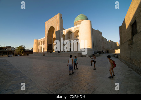 Les garçons jouent au soccer (football) par le minaret kalon et le Mir-i-Arab medressa à Boukhara. Banque D'Images