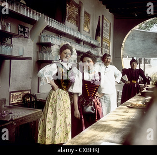 Photo colorisée de trois barmaids et d'un barman debout derrière un bar d'une auberge Alpine, Suisse, 1904. (Photo de Burton Holmes) Banque D'Images