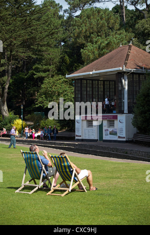 Couple assis dans des chaises longues regardant le groupe dans le kiosque dans les jardins de Bournemouth en Août Banque D'Images