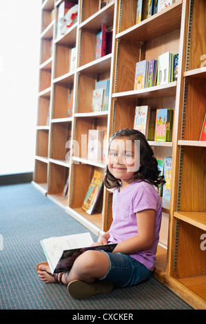 Mixed Race girl reading book in library Banque D'Images