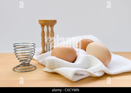 Still Life image de sablier, le sable d'oeufs egg cup sur serviette sur le haut de planche à découper en bois sur un fond blanc. Banque D'Images