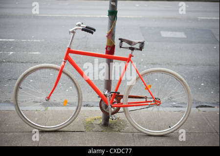 Pignon fixe de vitesse unique Orange vélo de course avec des pneus blancs enchaînés à un lampadaire de la ville avec des graffitis. Banque D'Images