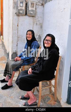 Deux vieilles dames s'assoient à l'extérieur de leurs maisons et parlent dans une allée ombragée, loin des intenses températures de Junes à Pano Elounda, en Crète, en Grèce Banque D'Images