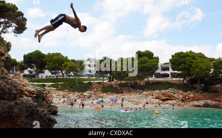 Cala D'Or, adolescent saute d'une falaise dans l'eau Banque D'Images