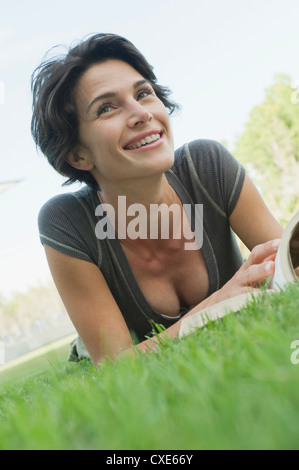Woman lying on grass avec livre, smiling Banque D'Images