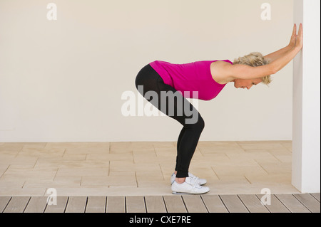 Mature Woman stretching contre mur, side view Banque D'Images