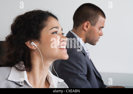 Woman listening to earphones et rêvasser dans office Banque D'Images