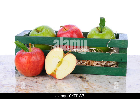 Une caisse en bois avec un assortiment de pommes sur une table en granit avec une tranche de pomme à l'avant. Format horizontal avec un fond blanc. Banque D'Images