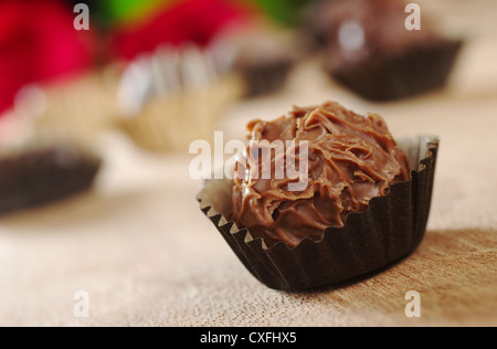 Libre d'une truffe au chocolat au lait avec l'emballage, avec d'autres truffes et roses rouges à l'arrière-plan photographié sur bois Banque D'Images