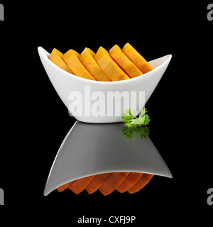 Tranches de pommes de terre sucrées cuites (lat. Ipomoea batatas) dans un bol blanc garni d'une feuille de persil et photographié sur noir Banque D'Images