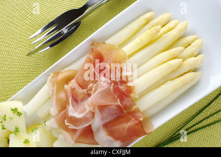 Asperges Blanches cuites fraîches servies avec du jambon et pommes de terre sur la plaque avec la ciboulette et les couverts sur les côtés Banque D'Images