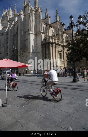 Man and Woman riding Sevici de location de vélos communautaires dans la Plaza Virgen de los Reyes par la Cathédrale de Séville Espagne Banque D'Images