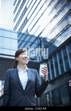 Une femme d'affaires avec une tasse de café entre les immeubles de bureaux à travers Banque D'Images