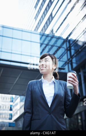 Une femme d'affaires avec une tasse de café entre les immeubles de bureaux à travers Banque D'Images