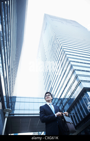 A smiling business man walking entre les immeubles de bureaux avec un porte-documents à la recherche autour de Banque D'Images