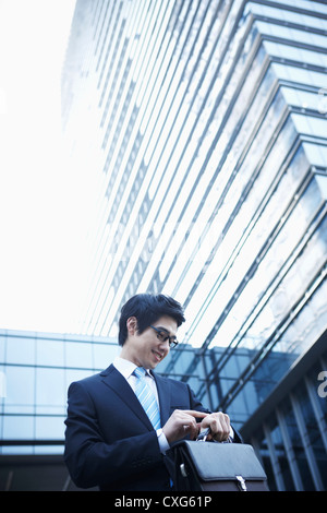 A smiling business man walking entre des immeubles de contrôler l'heure sur sa montre Banque D'Images