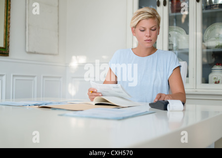 Jeune femme blonde cette vérification et l'utilisation de calculatrice à la maison Banque D'Images