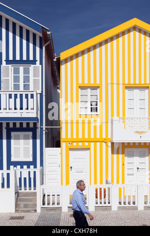 Un homme marche par les bonbons colorés traditionnels maisons de plage à rayures en Costa Nova, Beira Litoral, Aveiro, Portugal Banque D'Images