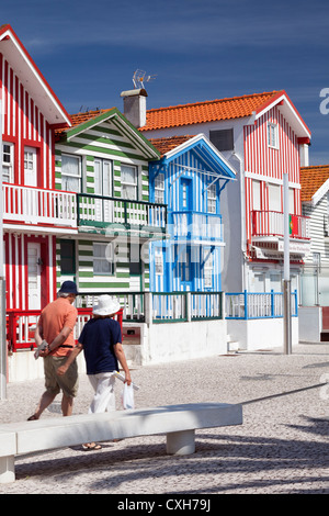 Un couple marche par le traditionnel coloré à rayures bonbon maisons de plage à Costa Nova, Beira Litoral, Aveiro, Portugal Banque D'Images