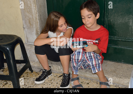 De jeunes enfants jouant dans la console de jeu de poche porte dans la vieille ville de Corfou, Kerkyra, Corfou, îles Ioniennes, Grèce Banque D'Images