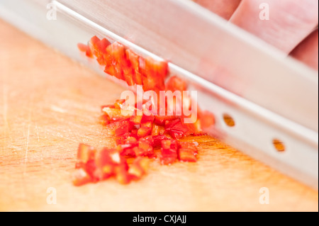 Gros plan du piment rouge haché en cours par un chef cuisinier sur une planche à découper en bois Banque D'Images