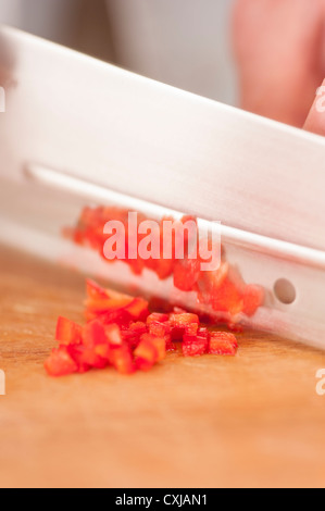 Gros plan du piment rouge haché en cours par un chef cuisinier sur une planche à découper en bois Banque D'Images