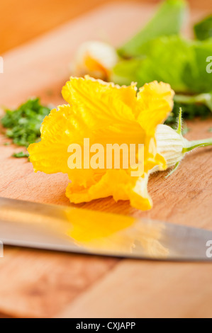 Fleur de courgette et couteau de cuisine sur une planche à découper en bois Banque D'Images