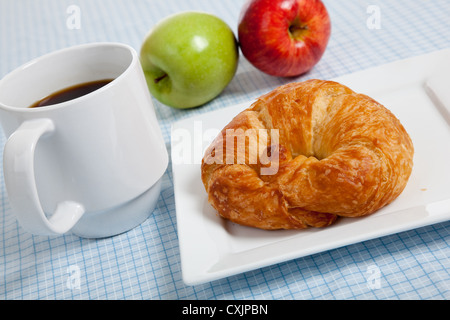 Croissant français sur une plaque blanche avec tasse à café et pommes sur une nappe Vichy bleu Banque D'Images