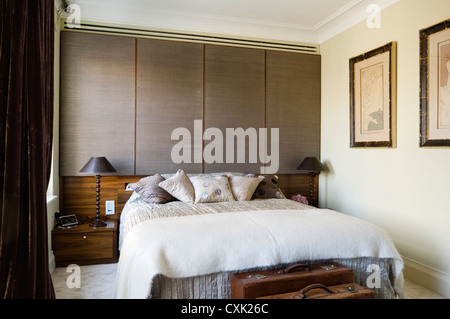 Intérieur couleur jour chambre lit double lit couette couverture oreiller soie texturée correspondant table de chevet lampe valise bagages artwork Banque D'Images