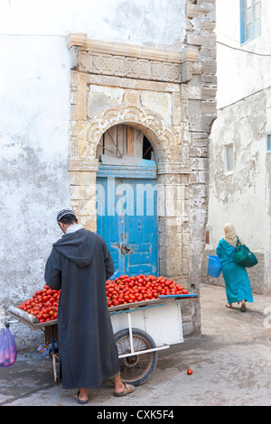 Dans l'homme marocain kaftan et tomates de vente chapeau panier dans la rue, Essaouira, Maroc Banque D'Images