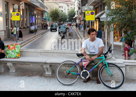 Un jeune homme est assis sur un banc avec son vélo. Il se trouve sur la promenade où il peut voir les gens de quitter la plage. Banque D'Images