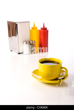 Plein jaune tasse à café avec sel et poivre shaker, porte-serviettes et la moutarde et du ketchup sur un fond blanc Banque D'Images