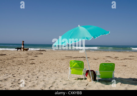 La Californie, la côte du Pacifique, Pismo Beach. Parasol et chaises vides sur Pismo State Beach. Woman walking dogs. Banque D'Images