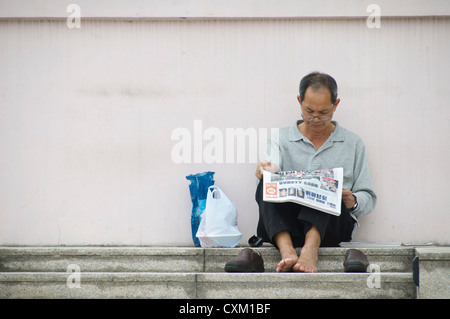 Hong kong local homme lisant le journal tout en vous relaxant dans la région de Wan Chai. Banque D'Images