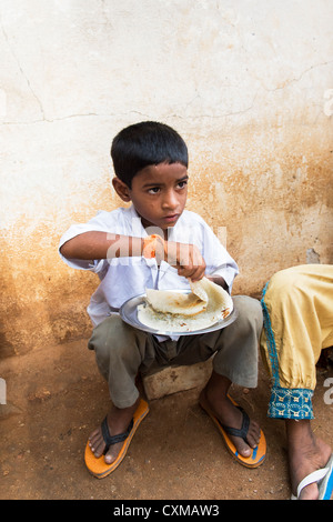 Basse caste indien boy eating dosa pour le petit-déjeuner dans une rue. L'Andhra Pradesh, Inde Banque D'Images