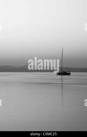 Vue d'un voilier amarré sur l'eau à l'aube. Le mât du bateau se reflète dans l'eau Banque D'Images