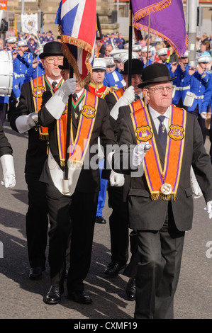 Un certain nombre des orangistes, vêtu du costume traditionnel 'Orange' ceinture chapeau melon et marcher sur une route pendant une parade de l'ordre d'Orange Banque D'Images