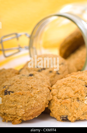 Des délicieux cookies à l'avoine et aux raisins s'échappant d'un récipient en verre avec un fond jaune. Banque D'Images
