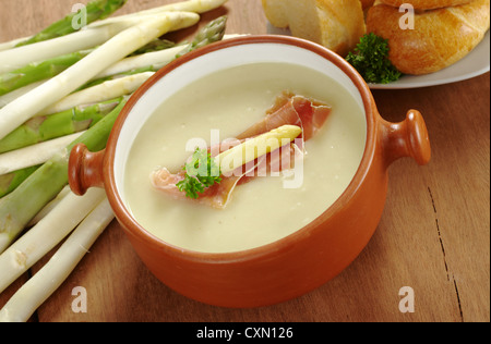 Bol de soupe aux asperges rustique garnie de jambon, le persil et la tête d'asperges accompagnée de pain avec des asperges sur le côté Banque D'Images