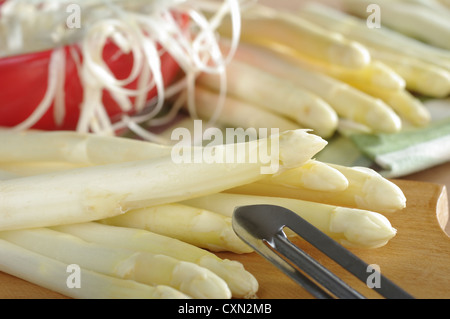 L'asperge blanche avec peeler sur planche de bois avec des asperges et un bol plein de rouge à l'arrière de Peel Banque D'Images