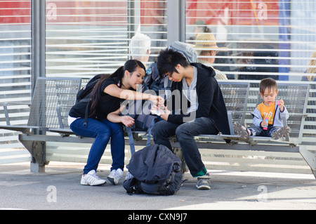 Jeune couple avec enfant s'asseoir sur le banc de la plate-forme de la gare de petit garçon souffle des bulles de savon, principale gare ferroviaire de Heilbronn Banque D'Images