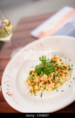 Un bol de risotto fraîchement préparé servi avec un verre de vin blanc sur une table à l'extérieur dans un restaurant à Cornwall Banque D'Images