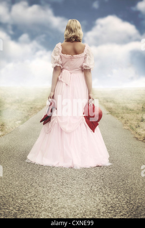 Une femme dans une robe est de marcher le long d'une route avec ses chaussures et son chapeau dans ses mains Banque D'Images