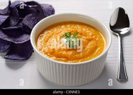 Soupe de carottes à la crème et le persil dans un bol blanc avec blue chips de pomme de terre et la cuillère Banque D'Images